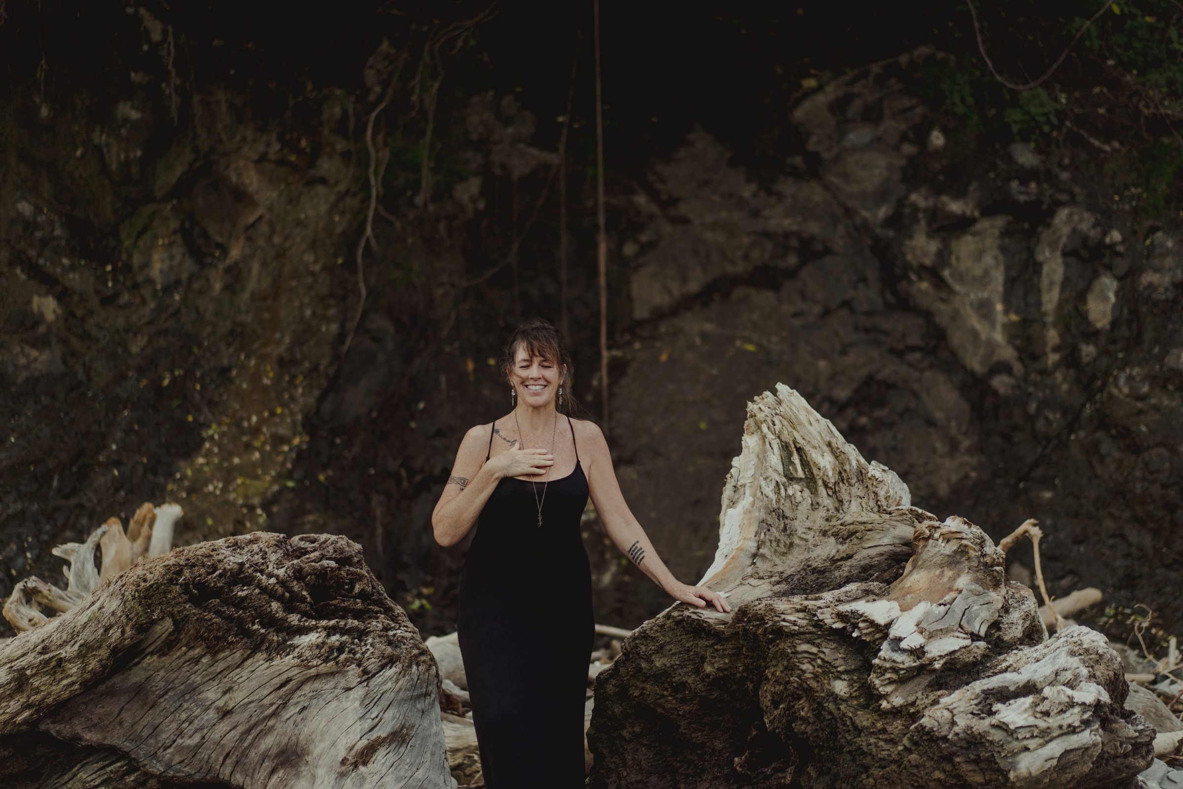 Kerry in a black dress among driftwood on the beach